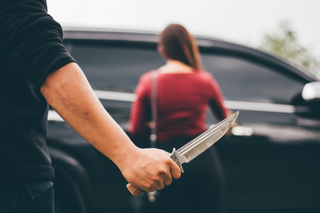 hand of criminal or bandit hold a knife trying to rob money and hurting woman when she open the car door.の写真素材