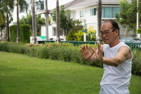 asian senior man wear white shirt stand and practice tai chi on the grass in the gardenの写真素材