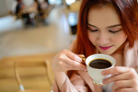 Portrait of beautiful face woman and hand holding a cup of coffee in her hand in blur background coffee shop, she drink coffee in the morningの写真素材