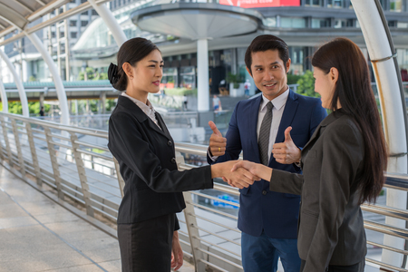 business man show thumb up and two business woman shaking hands for demonstrating their agreement to sign agreement or contract between their firms, companies, enterprises. success conceptの写真素材