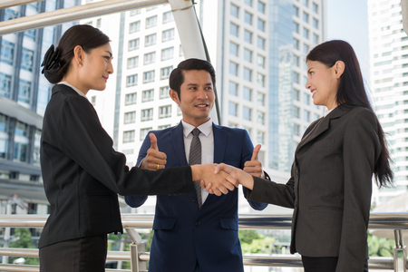 business man show thumb up and two business woman shaking hands for demonstrating their agreement to sign agreement or contract between their firms, companies, enterprises. success conceptの写真素材