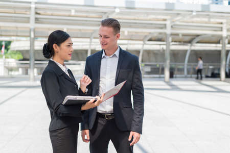 Asian businesswoman and Caucasian businessman discussion business issue from financial report on paper, they are standing in the city and buildings background.の写真素材
