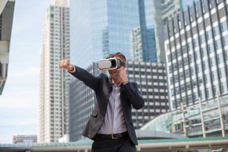 Caucasian Businessman wear black suit and Virtual Reality Headset (VR) and fighting by punch to the airの写真素材