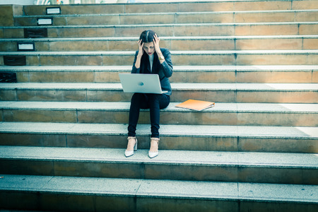 A businesswoman sit on the stairs and her hands clasped head,the feeling of stressed, sadness or displeasure caused by the non fulfillment of one's hopes or expectations.の写真素材