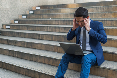 A businessman sit on the stairs and his hands clasped head,the feeling of stressed, sadness or displeasure caused by the non fulfillment of one's hopes or expectations.の写真素材