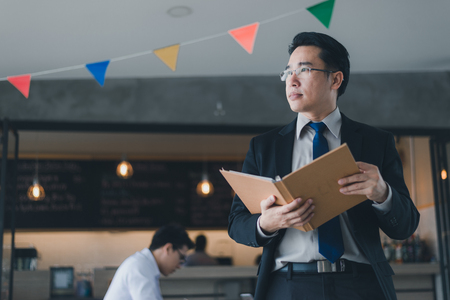 Asian businessman in black suit, who standing and holding document file about financial report on hand.の写真素材