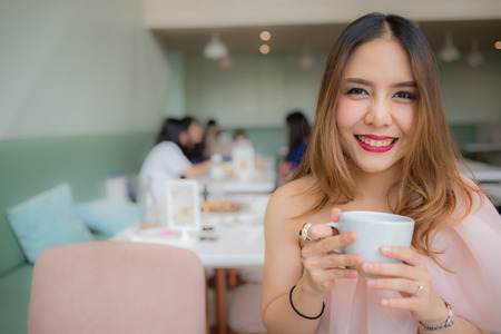 beautiful woman smile and holding a cup of coffee in her hand on blur background coffee shopの写真素材
