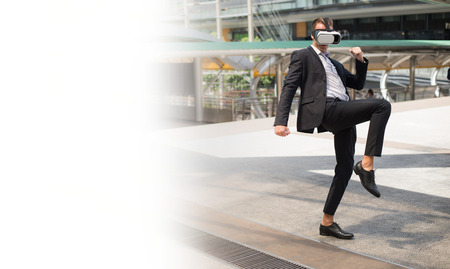 Caucasian Businessman wear black suit and Virtual Reality Headset (VR) and fighting by kick to the airの写真素材