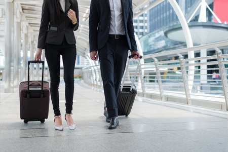 businessman and businesswoman walk together with mobile tablet and luggage on the public street, business travelの写真素材