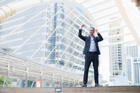 caucasian businessman smile and raising up two hands to cheerful and celebrated his successful in career and mission. concept of winner and competition with copy space for text.の写真素材