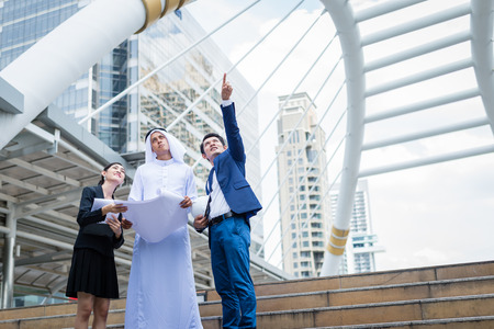 arab businessman holding blueprint on hand and talk about construction process with Asian businessman and businesswoman in the city.の写真素材