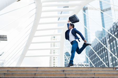 Motion blurred of Asian businessman, who holding briefcase and jumping in the city to cheerful and celebrated his successful in career and mission. concept of winner and competitionの写真素材