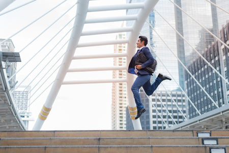 Asian businessman in formal wear holding briefcase while running and jump in the city on a background of building. late for work conceptの写真素材