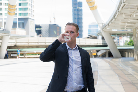 Caucasian businessman drinking pure mineral water from plastic bottle in hot summer day with background of city.の写真素材