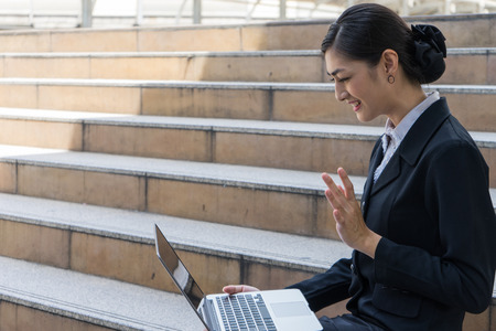 business woman smile and sit on the staircase with laptop, she happy because she talk with friend by video callの写真素材