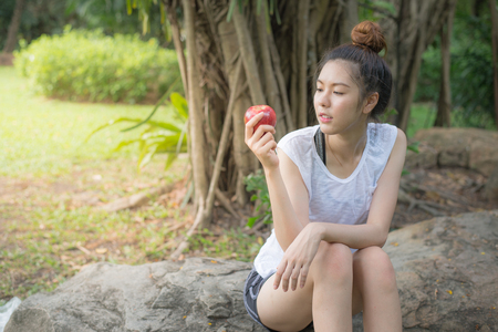 woman sitting on the stone at garden and eating red apple after exerciseの写真素材