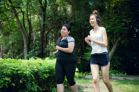 fat woman and thin woman exercise by jogging in the garden, they are running for health and lose weight.の写真素材