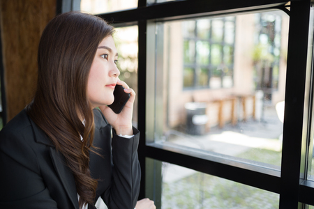 beautiful woman talk with friend via mobile phone near glass window with copy space for text.の写真素材