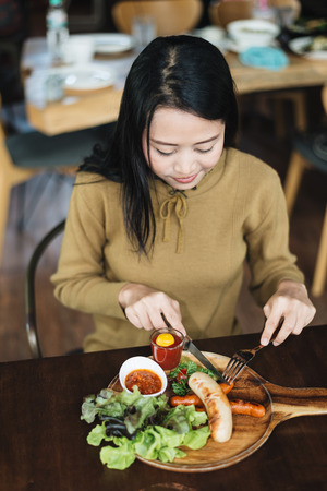 Woman holding knife and fork for eating food, Sausage with Tomato Sauce and green vegetable on wood plateの写真素材