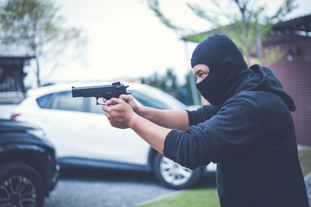 Criminal or Bandit wear black mask and clothes using gun point to somewhere, concept of criminal, bandit, gangster, mafiaの写真素材