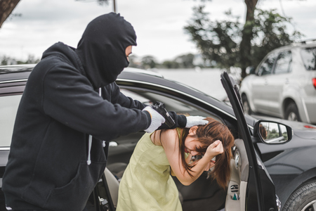 Criminal or Bandit wear black mask and black clothes using gun point to woman in car and trying to rob money and hurting herの写真素材