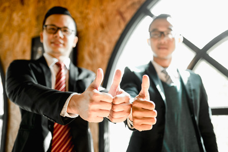 two businessman stand and show thumb up their hand to demonstrating their agreement to sign agreement or contract between their firms companies enterprises. successful conceptの写真素材