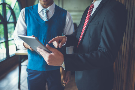 Two businessman standing and looking to tablet, they are meeting and talking about business plan, marketing and financial in the future. they are looking and point finger to detail in notebook, concept of business success.の写真素材