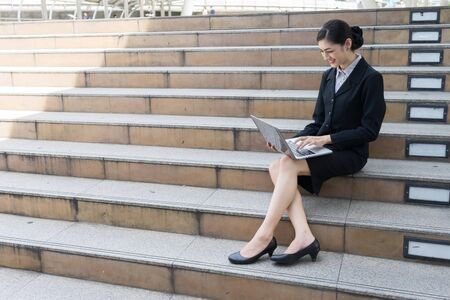 Asian businesswoman smile and sit on the staircase, she typing word into laptopの写真素材