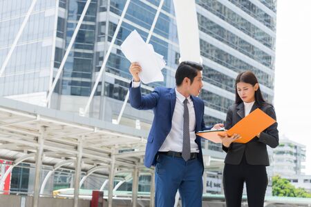 Angry businessman stand and holding document on hand, he blaming secretary for work mistakes.の写真素材