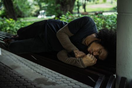 Poor homeless man or refugee sleeping on a seat in the park. social documentary concept.の写真素材