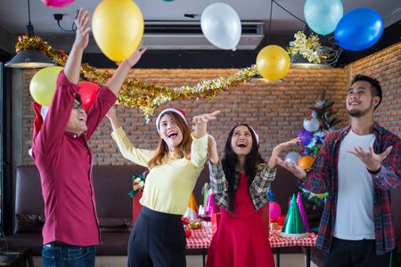Asian man and woman wear santa claus hat having fun in Christmas party,dancing and playing balloons at the restaurant, Concept of Christmas party or New Year's party.の写真素材
