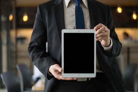 businessman wear black suit holding a tablet with blank screen in the office. with black copy space...