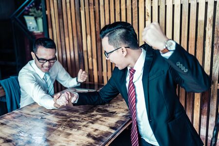 two businessman expressed a serious expression and fighting by used arm wrestling on wood table. one...