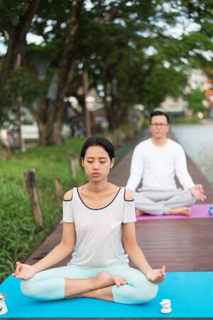woman and man practicing yoga and meditation on mat near lagoon. health concept.の写真素材