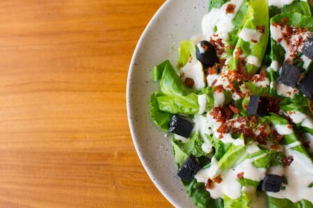 Vegetable salad, add salad dressing, sprinkle with black bread on a white plate, see half a plate placed on a wooden table.の写真素材