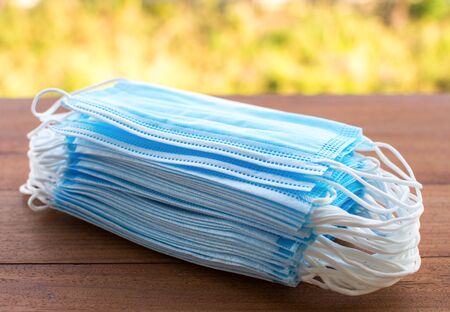 Many blue medical protective masks are laid on the wooden floor. Covering the mouth and nose,...