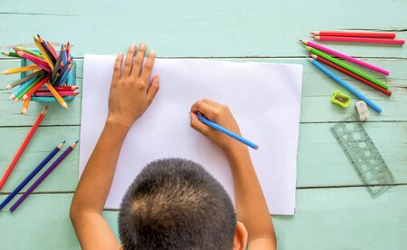 The top view of the boy uses colored pencils to draw on white paper.
