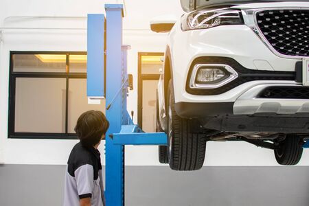 The mechanic was looking at the white car that was lifted for repair in the car center.の写真素材