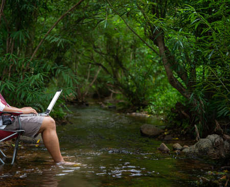 A young man with a laptop in the middle of nature, rivers, mountains and forests.
