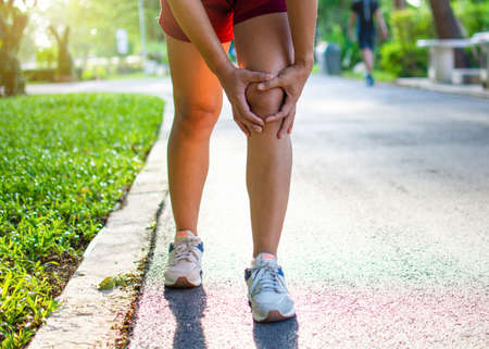 Exercise concept injury: Asian woman grasping her knees while running on park street. Taken in the...