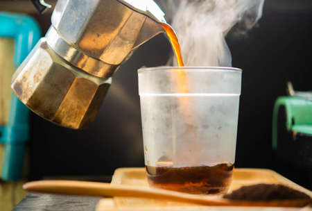 Hot coffee is poured from a freshly brewed coffee pot into a mug that sits on the table with white smoke from the heat.の写真素材