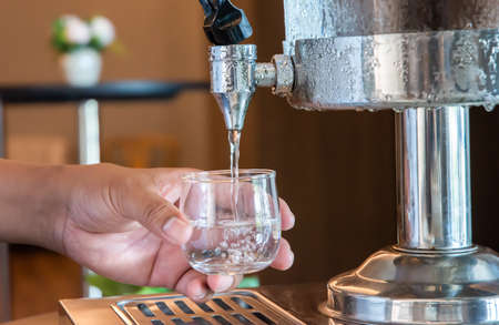 Water is poured into a glass from a manual water dispenser in the hotel restaurant.