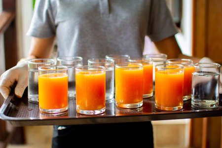 A glass of orange juice and a glass of water on a stool served to the hotel guestsの写真素材
