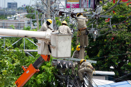 Four electric workers climbed a pole and used a cable car to maintain a high voltage line system on a dangerous electric pole in Nonthaburi province. Thailand Date 06-08-2020のeditorial素材