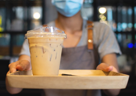 The waiter serves iced lattes on a wooden tray for customers ordering in the coffee shop.