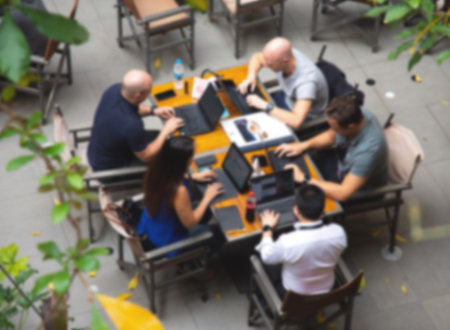 A blurry group of people sitting in front of computers on a coffee shop table.の写真素材