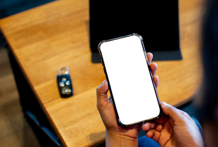 White blank smartphone mobile screen in the hand of a woman at a table in a cafe