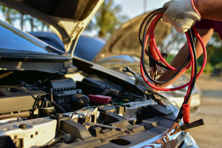 A mechanic carries a car battery charger to charge electricity through a jumper cable to another car on a country road.の写真素材