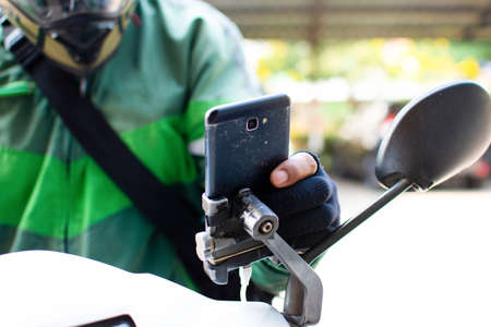 The hand of the food delivery attendant is pressing the smartphone on the motorbike to accept the online customer order.の写真素材