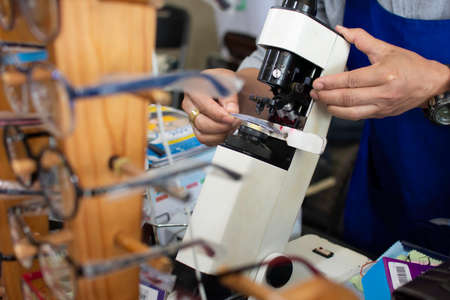 A skilled technician uses a microscope to look at the eyeglasses lenses. To measure the size for the customer at the eyeglass shopの写真素材